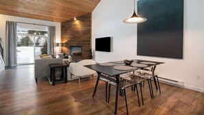 A modern living room with a wooden ceiling, a fireplace, a dining table with chairs, and a large abstract painting on the wall. - The Drift at Firelight | Big Sky Adventure+Hot Tub (Big Sky)
