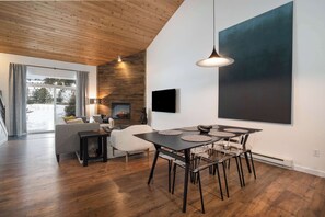 A modern living room with a wooden ceiling, a fireplace, a dining table with chairs, and a large abstract painting on the wall. - The Drift at Firelight | Big Sky Adventure+Hot Tub (Big Sky)