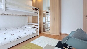 A bunk bed with a white and patterned bedding, a wooden wardrobe with a mirror, and a light blue chair with a grey cushion. - Familienfreundliche und gemütliche 3.5 Wohnung mit Garten by Interhome (Laax)