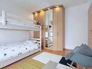 A bunk bed with a white and patterned bedding, a wooden wardrobe with a mirror, and a light blue chair with a grey cushion. - Familienfreundliche und gemütliche 3.5 Wohnung mit Garten by Interhome (Laax)