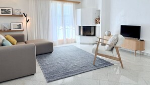 A modern living room with a sofa, a TV, a fireplace, and a large window with sheer curtains. - Familienfreundliche und gemütliche 3.5 Wohnung mit Garten by Interhome (Laax)