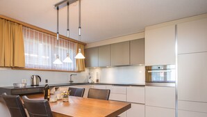 A modern kitchen with a wooden dining table, black chairs, and stainless steel appliances. - Top Ferienwohnung Breithorn (SkiIn/SkiOut) by Interhome (Zermatt)