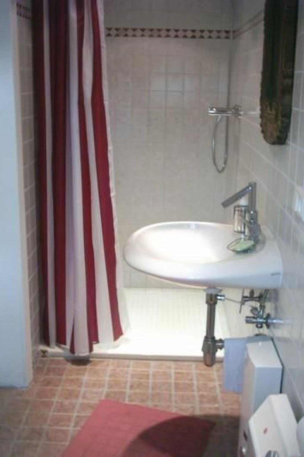 Ein Badezimmer mit einem weißen Waschbecken, einer Dusche und einem roten und weißen Streifenvorhang.