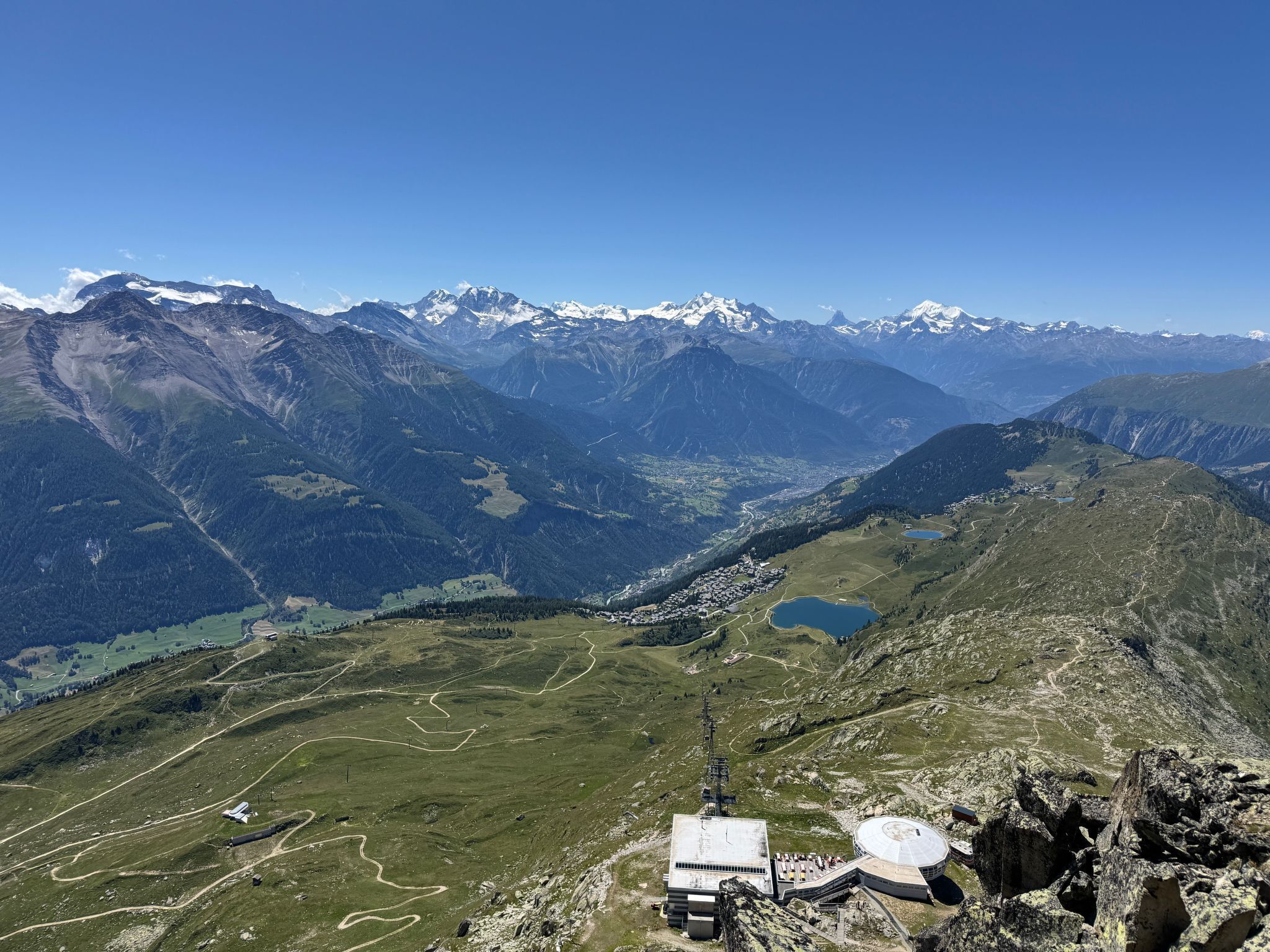 A mountainous landscape with a small building featuring a circular observation area and a rectangular structure with a flat roof.