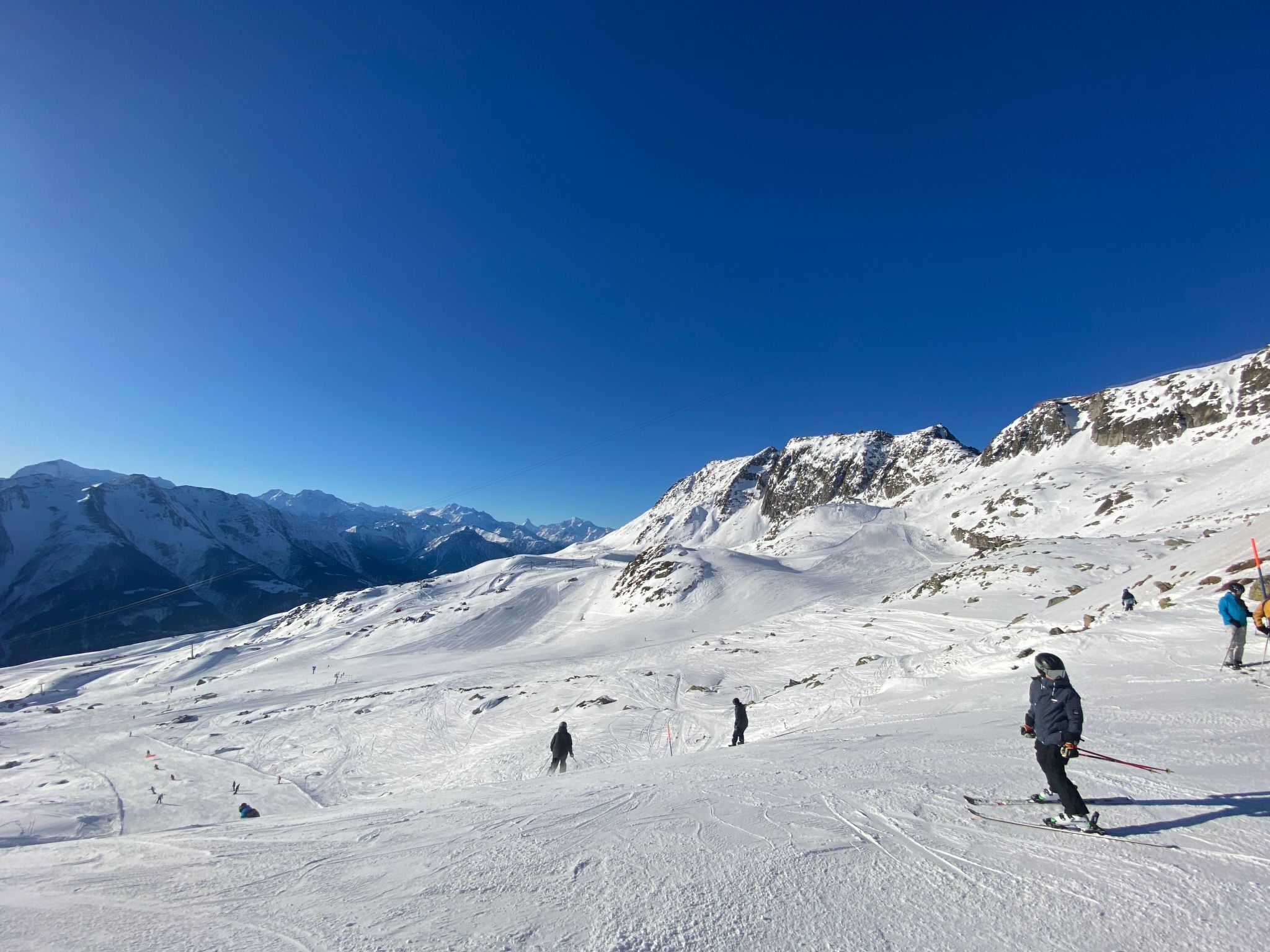 A snowy ski slope with skiers and a clear blue sky.