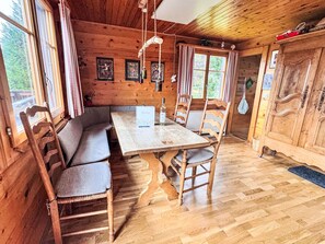 Interior de una cabaña de madera con una mesa de comedor, bancos y una zona de cocina.
