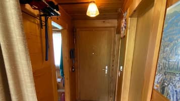 A narrow wooden hallway with a wooden door at the end, a light fixture above, and a shoe rack on the left.