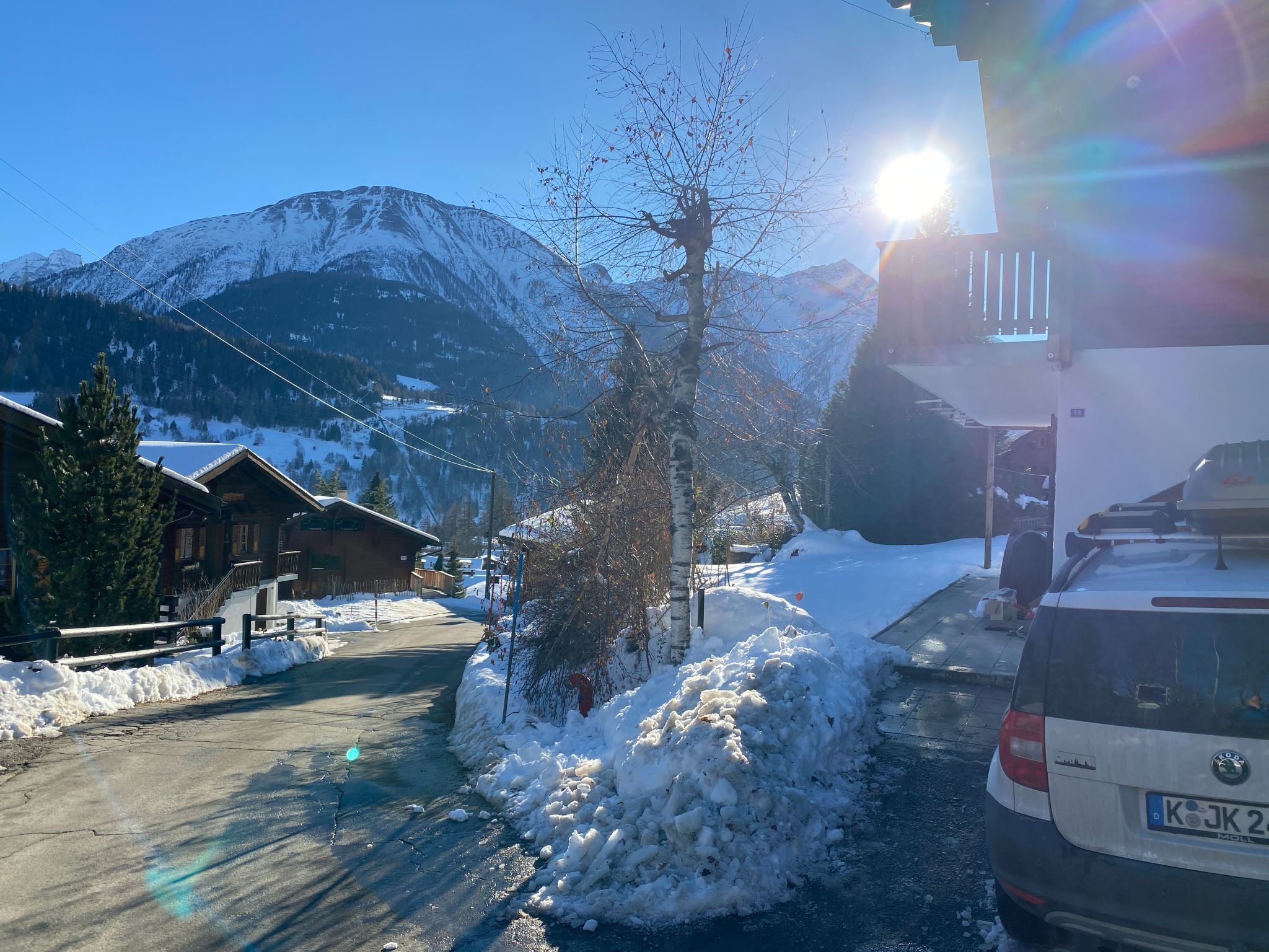 A snowy mountain village with wooden houses, a car, and a clear sky.
