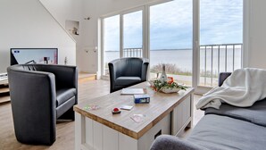 Ein modernes Wohnzimmer mit Couchtisch aus Holz, zwei schwarzen Stühlen, einem grauen Sofa und einem Fernseher, der eine Stadtansicht zeigt.