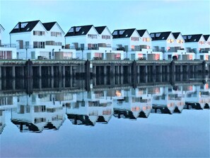 A row of white houses with dark roofs, reflected in calm water. - Fewo Kapteins Lounge by Seeblick Ferien ORO by Interhome (Hasselberg)