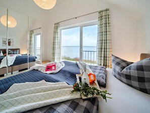 A bedroom with a large bed, a bedside table, a mirror, and a window with a view of the sea. - Fewo Kapteins Lounge by Seeblick Ferien ORO by Interhome (Hasselberg)