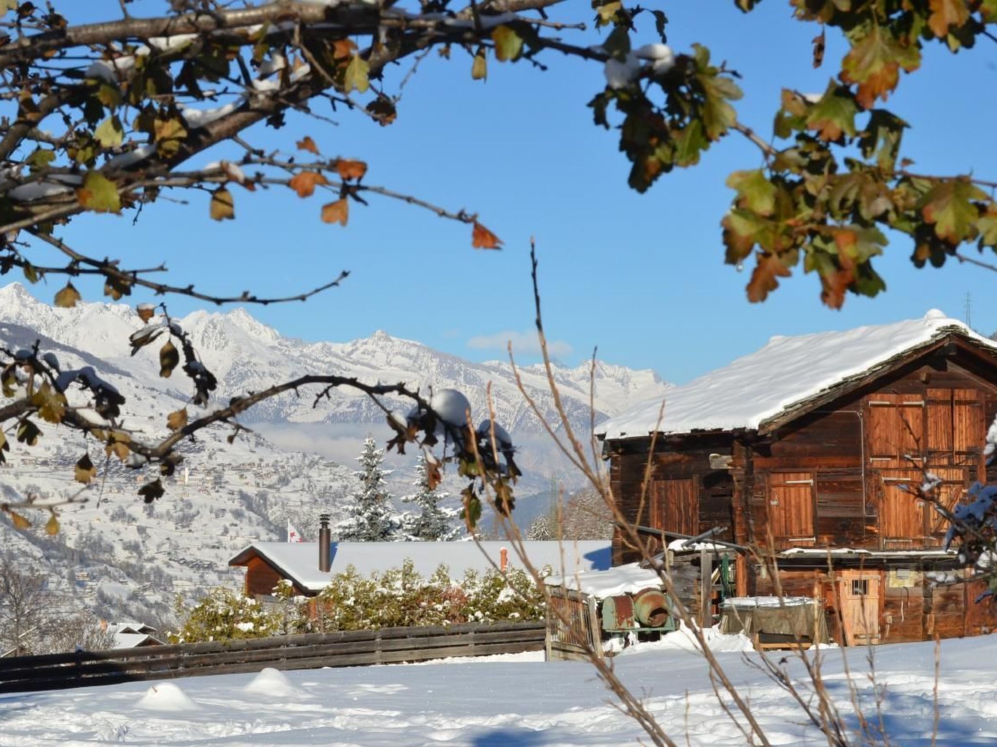 Eine Holzhütte mit schneebedecktem Dach, umgeben von einem Holzzaun, mit einem Gebirge im Hintergrund.