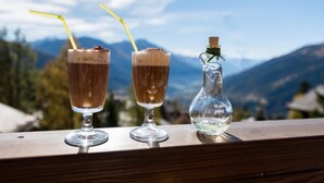 Dos vasos de una bebida oscura con pajitas, una botella transparente con corcho y un paisaje montañoso al fondo.