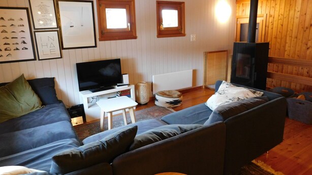 Ein gemütliches Wohnzimmer mit einem großen grauen Sofa, einem Flachbildfernseher, einem kleinen weißen Tisch und einem Kamin.