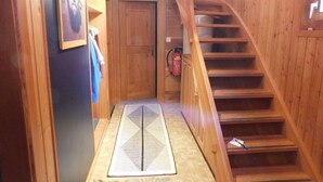 Eine Holztreppe führt zu einer Tür, ein Feuerlöscher und eine gemusterte Matte liegen auf dem Boden.