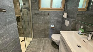 Un baño moderno con cabina de ducha de vidrio, inodoro y lavamanos con espejo.