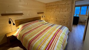 Un dormitorio con cabecera de madera, cama con colcha a rayas, lámparas de noche y una ventana con vistas al exterior.