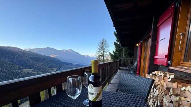 Un balcón con una botella de vino y copas, con vistas a un paisaje montañoso.