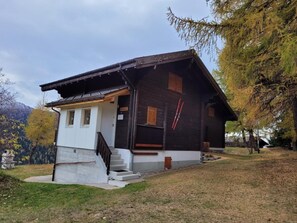 A wooden cabin with a white front section, a staircase leading to the entrance, and a ski rack on the side. - Chalet Männertreu OG by Interhome (Bellwald)
