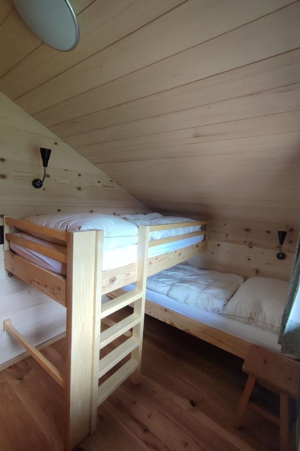 Ett rum med en våningssäng i trä, ett sluttande tak och en taklampa.