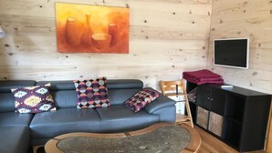 A cozy living room with a blue sofa, patterned cushions, a wooden coffee table, a television, and a wooden cabinet. - Chalet Männertreu OG by Interhome (Bellwald)
