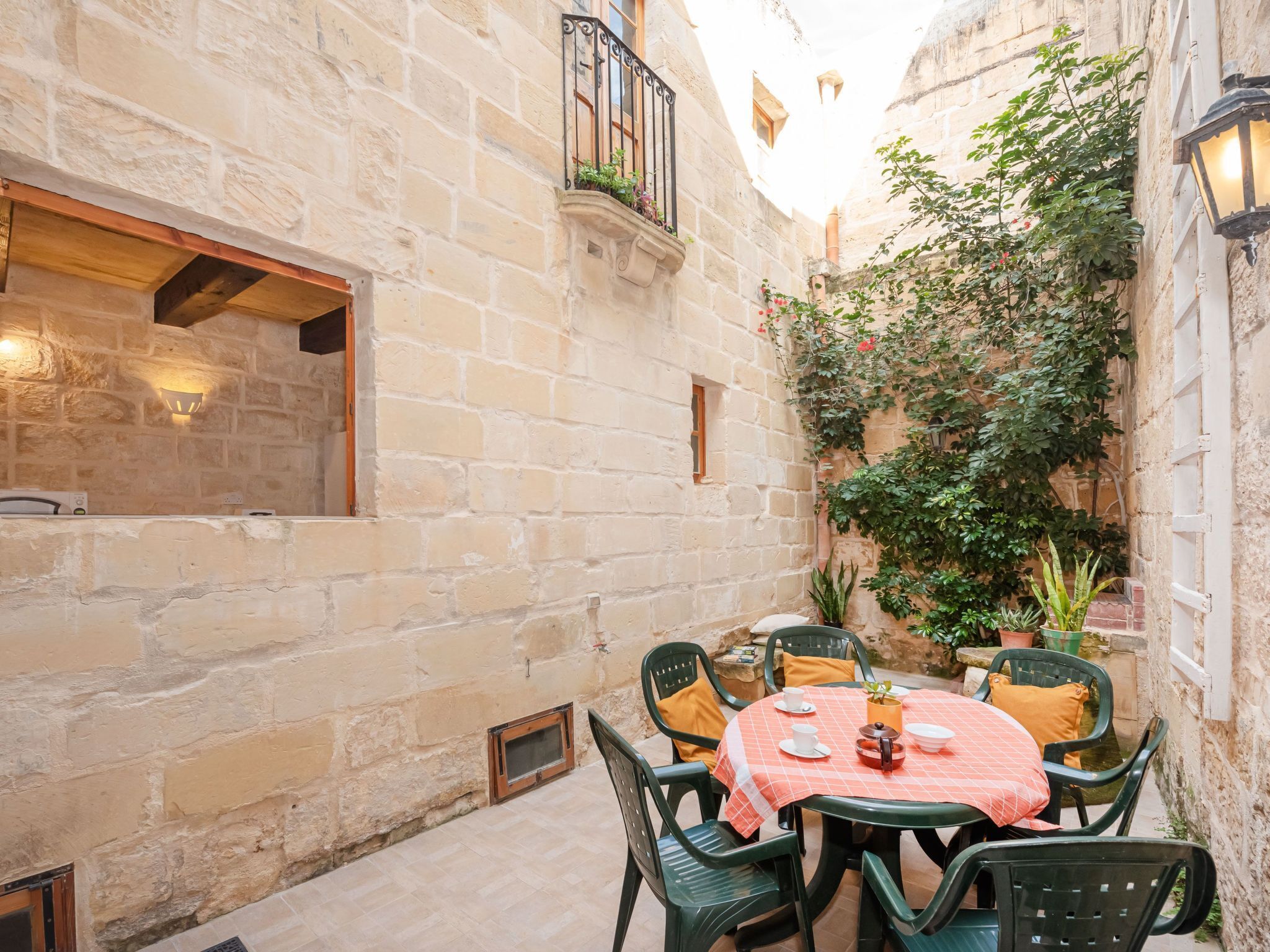 A stone-walled courtyard with a round table set for dining, surrounded by chairs.