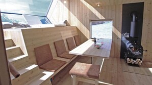 Interior acolhedor de uma cabana com um espaço de estar com bancos de madeira, uma mesa de jantar e uma lareira a lenha.