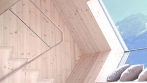 Uma escada de madeira leva a um espaço de loft com claraboia e vista para as montanhas.