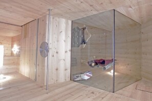 Interior de una cabaña de madera con un separador de vidrio, un poste de metal y un perchero colgante.