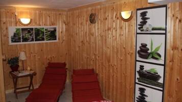 A room with wooden panel walls, two red massage beds, a wall-mounted clock, and a framed picture of stones and plants.