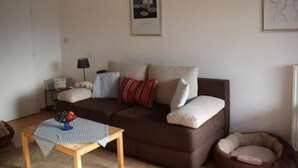 A living room with a brown sofa, a small wooden table with a checkered tablecloth, and a pet bed.