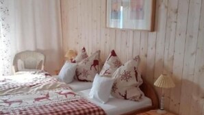 A wooden-paneled bedroom with a bed, pillows, a chair, a nightstand, and a framed picture on the wall.