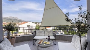 Un balcón con una mesa, dos sillas blancas con cojines y un toldo grande triangular.