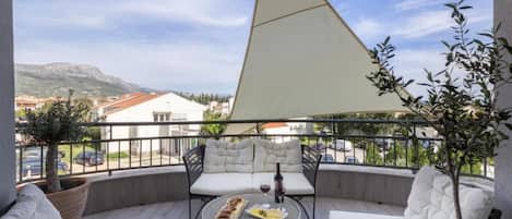 A balcony with a table, two white cushioned chairs, and a large triangular shade.