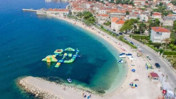 Vista aérea de un pueblo costero con una playa despejada, un pequeño muelle y un promontorio rocoso.