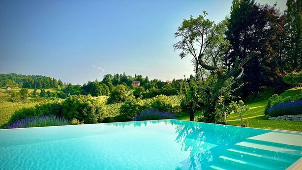 Una piscina infinita azul cristalina con vistas a un jardín exuberante y colinas distantes.