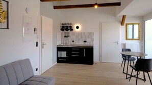 Eine moderne Küche mit Holzbalken, ein Essbereich mit rundem Tisch und Stühlen sowie ein graues Sofa.