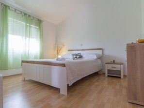 Ein Schlafzimmer mit einem Bett, einem Nachttisch, einem Holzschrank und einem Fenster mit grünen Vorhängen.