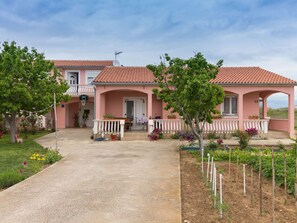 Eine pinkfarbene Villa mit einem Ziegeldach, einem Balkon und einem Garten mit verschiedenen Pflanzen und Blumen.