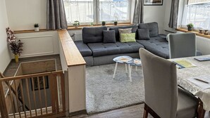 Ein modernes Wohnzimmer mit einem grauen Ecksofa, einem Esstisch mit Stühlen und einer Treppe zu einer oberen Etage.
