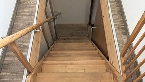Eine Holztreppe mit Handlauf, die zu einer Zwischenebene führt, auf der ein gerahmtes Bild an der Wand hängt.