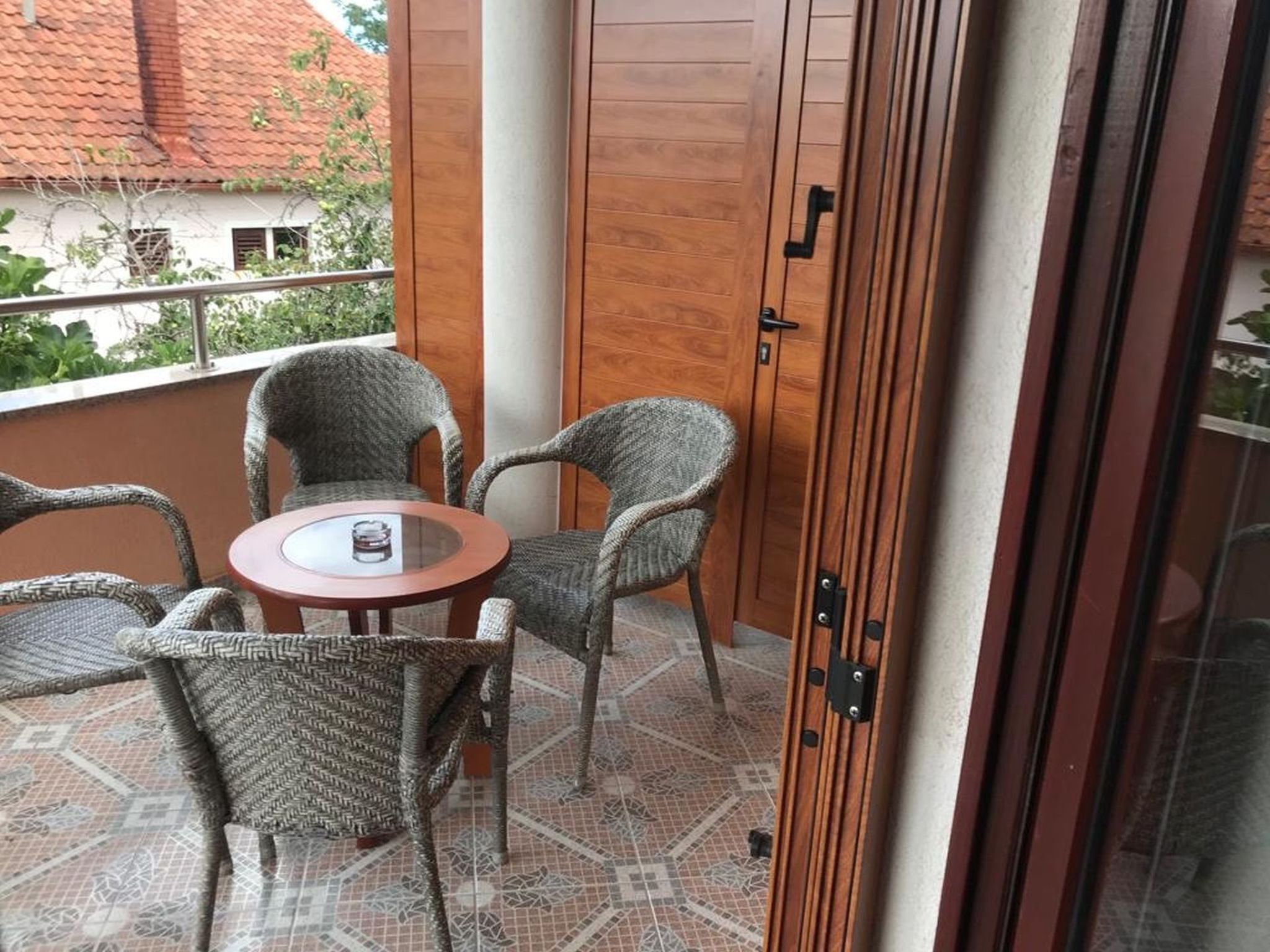 Ein Balkon mit Korbstühlen, einem kleinen Tisch, einer Holztür und einem gefliesten Boden.