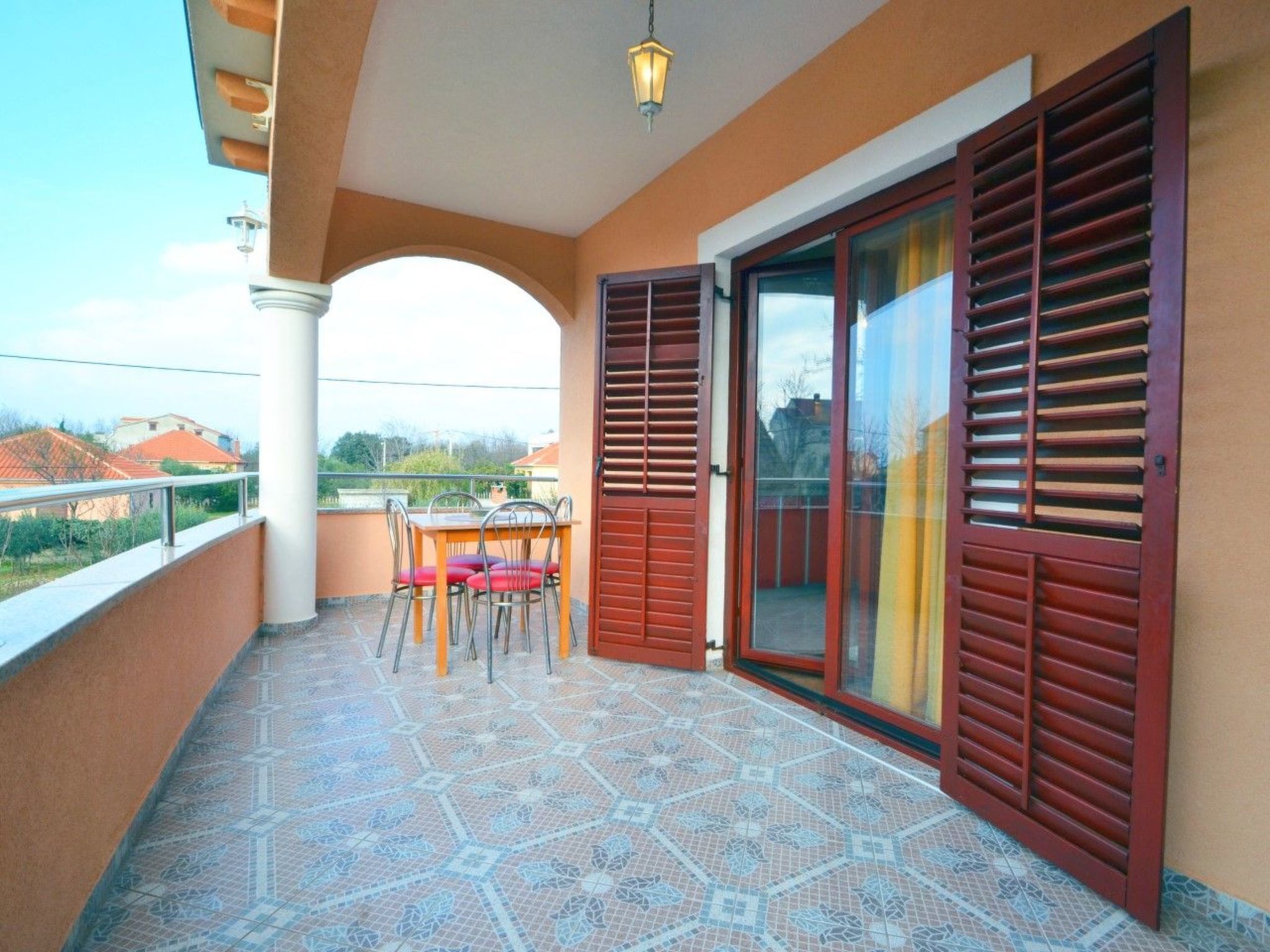 A balcony with a tiled floor, a table with chairs, and a sliding glass door with shutters.