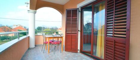 Ein Balkon mit Fliesenboden, einem Tisch mit Stühlen und einer Glastür mit Rollläden.