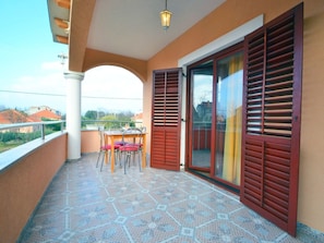 Un balcone con pavimento piastrellato, un tavolo con sedie e una porta scorrevole in vetro con persiane.