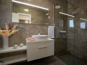 Ein modernes Badezimmer mit großem Spiegel, weißem Waschbecken und Duschkabine.