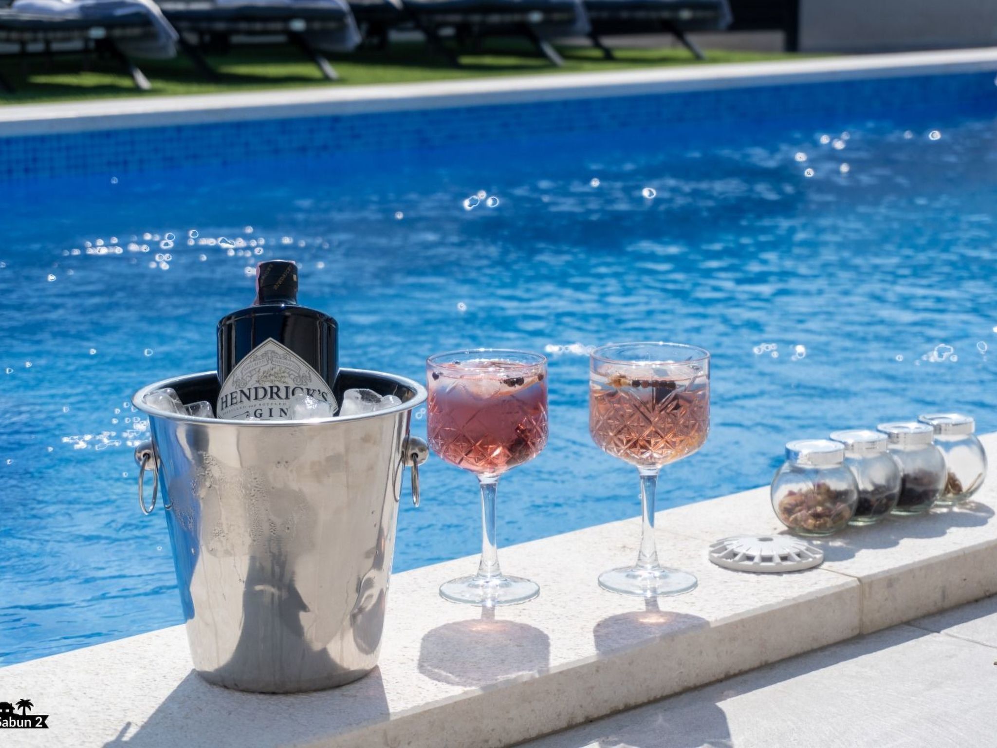 Et poolmiljø med en metalspand mærket "Hendrick's Gin" og to glas med lyserød cocktail.