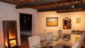 A cozy dining area with a glass table and chairs, a fireplace, and a bookshelf with books and decorative items.