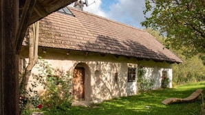 A rustic house with a tiled roof, a wooden door, and a small garden with a wooden bench.