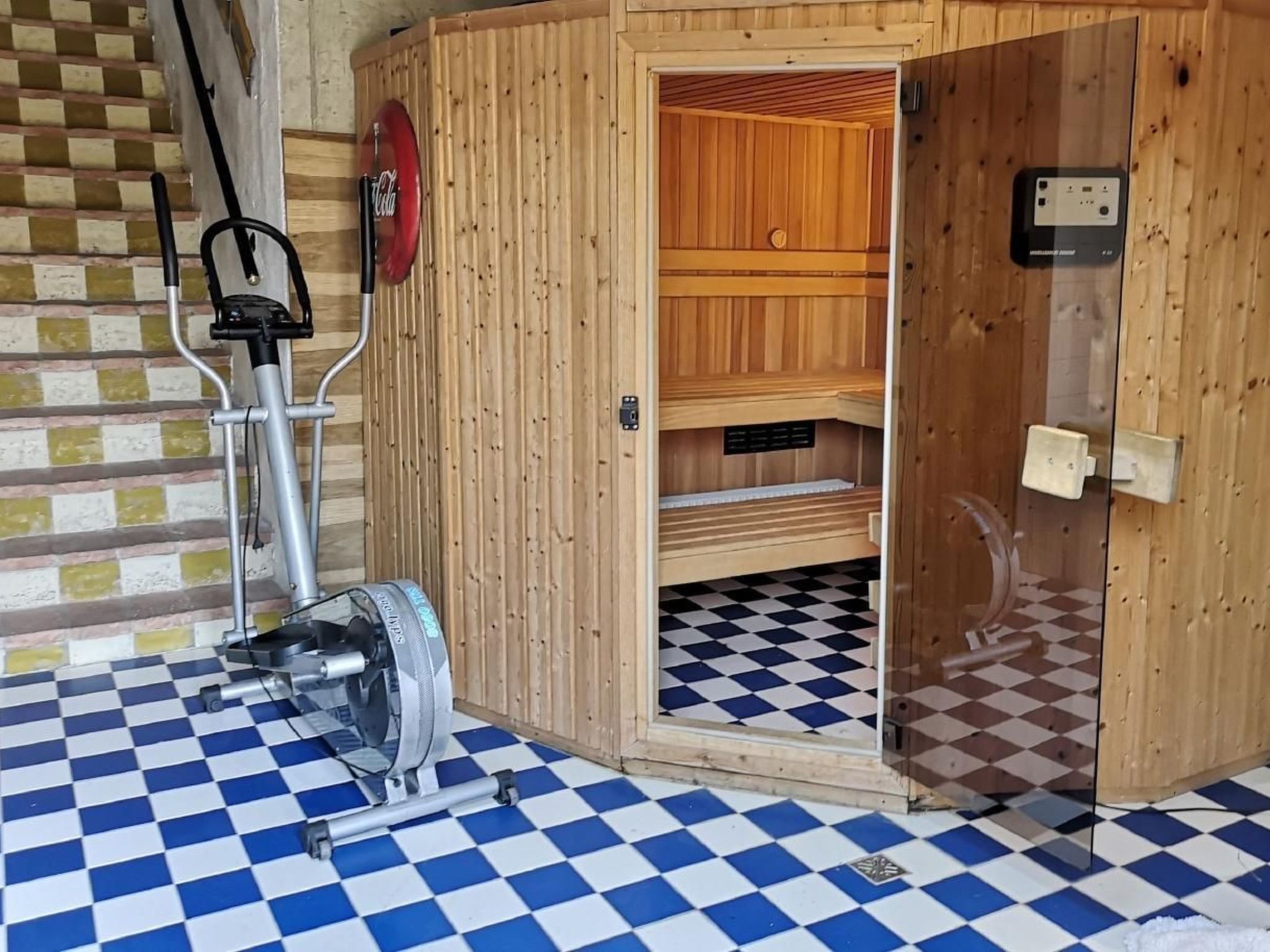Een sauna met een geruite vloer, een houten deur en een bedieningspaneel aan de muur.
